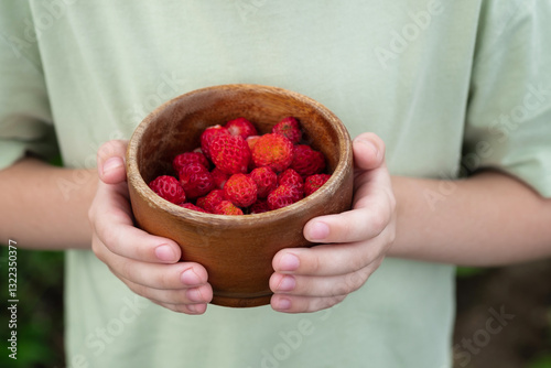 Child holding wooden bowl filled with fresh red strawberries