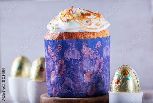 Easter cake, chocolate eggs in gold foil and chicken-shaped candles on a light background.