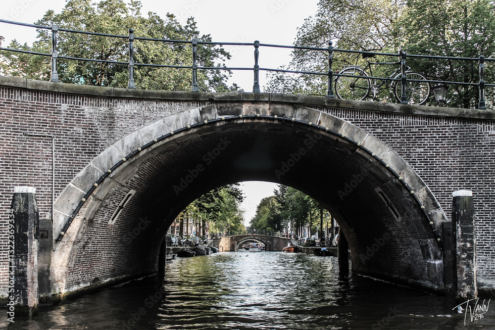 Fototapeta premium Amsterdam, Netherlands architectural photography, Amsterdam Canal with Historic Dutch Houses at Sunset, Cyclist Riding Through Amsterdam’s Charming Streets, Houseboats and Bridges Along the Amsterdam