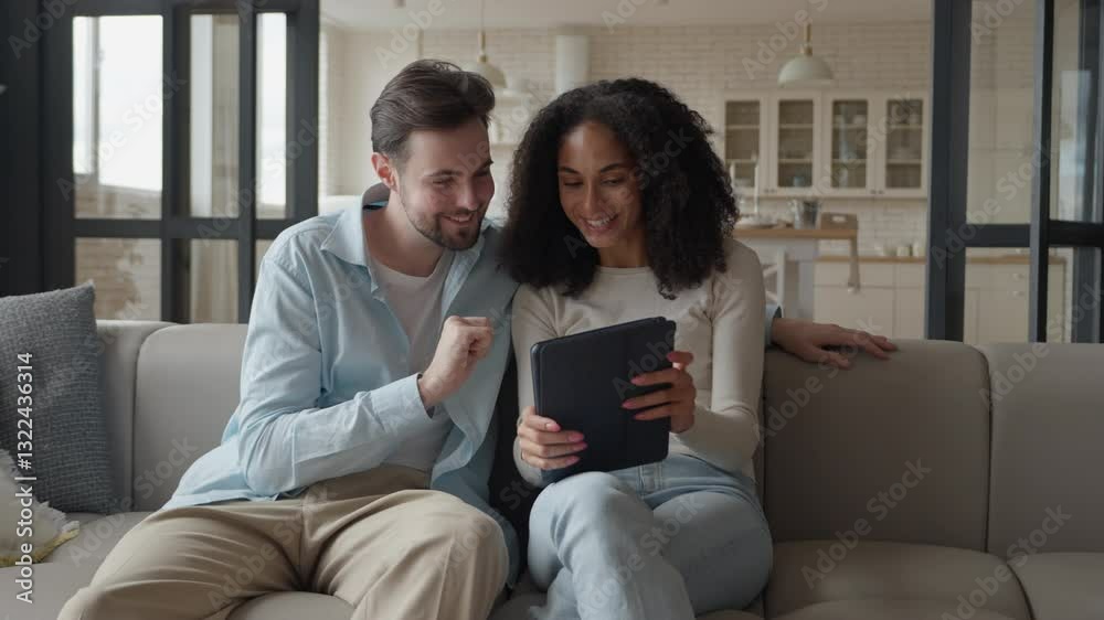 Smiling Couple Sitting On Sofa, Enjoying Content Together On Tablet In Cozy Home Smiling Couple Sitting On Sofa, Enjoying Content Together On Tablet In Cozy Home