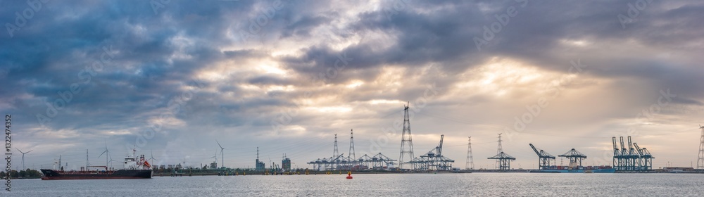 Fototapeta premium Cargo ship navigates through the bustling port of Antwerpen under a cloudy sky