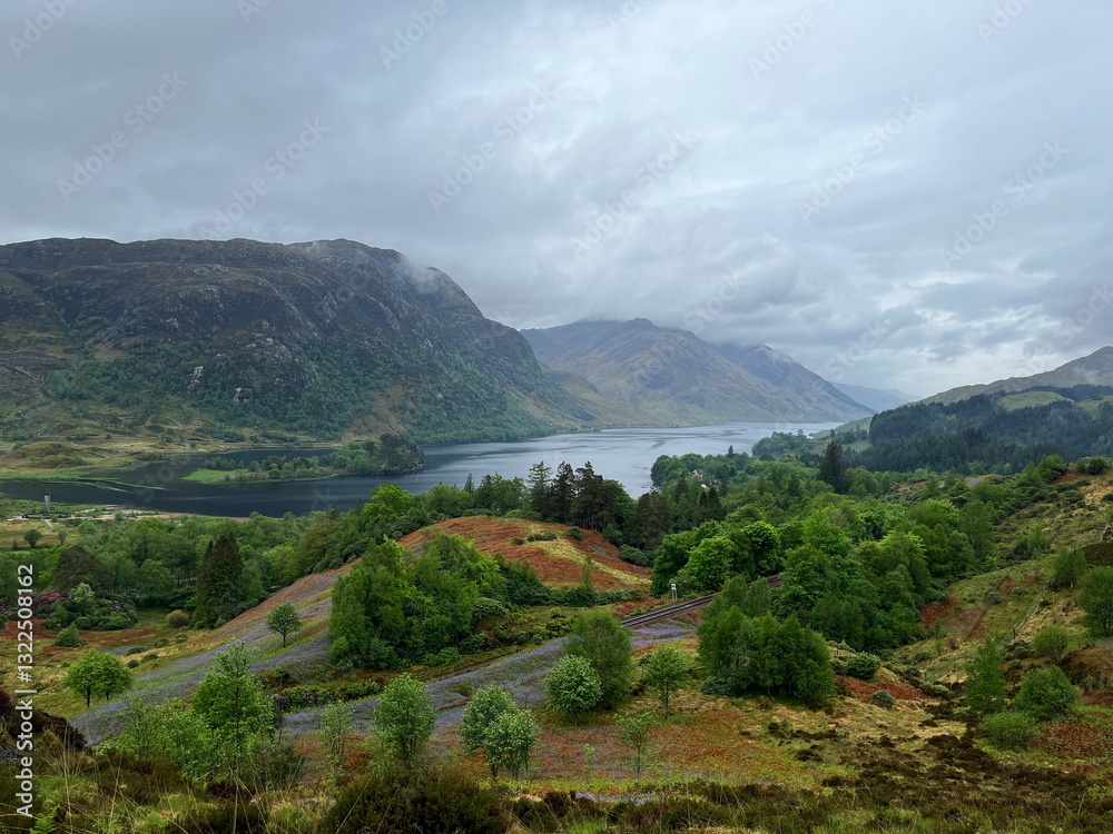 Fototapeta premium Stormy and rainy weather over Loch Shiel in the Scottish Highlands, with a cloudy sky, lush greenery and mountains surrounding the beautiful lake. Glenfinnan, Scotland, UK.