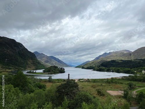 Glenfinnan Monument standing on the shore of Loch Shiel, surrounded by lush greenery and distant mountains, under a cloudy sky, creating a scenic spring landscape of the West Highlands, Scotland, UK. photo