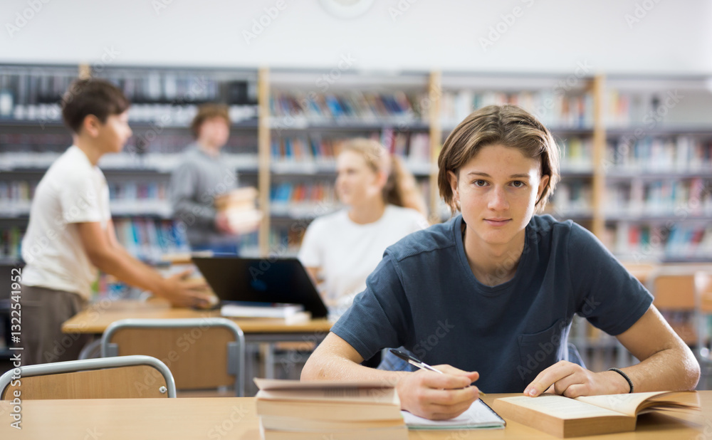 Fototapeta premium Teenage boy reading books and doing homework in library.