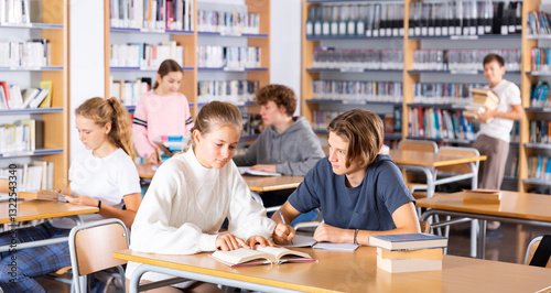 Group of intelligent girls and boys preparing for exams in library.