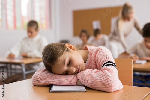 Portrait of tired school girl lying and sleeping at desk in classroom during lesson