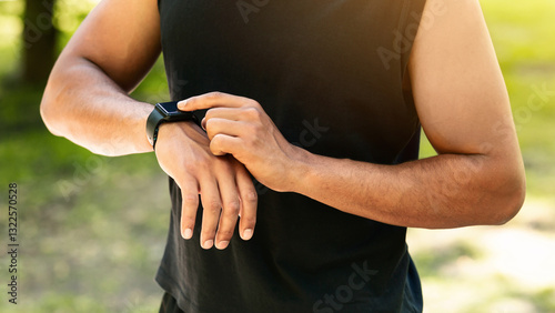 Closeup view of young guy checking his smartwatch or fitness tracker during training outdoors, panorama