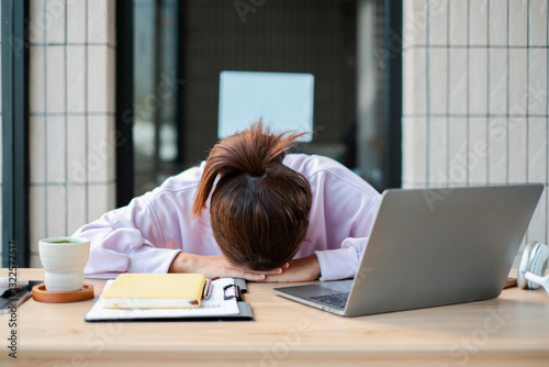 Tired woman in casual attire resting her head on a desk with a laptop and coffee, symbolizing workplace fatigue. photo