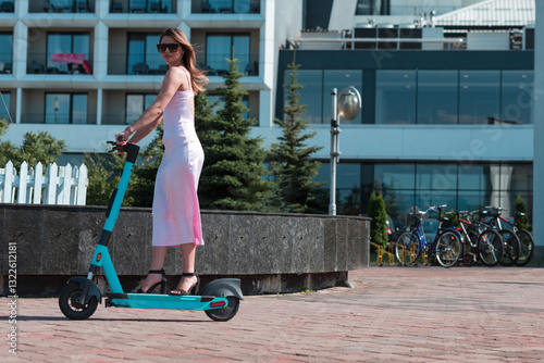 Elegant woman in a pink dress and sunglasses riding an electric scooter through the sunny city streets, embracing the freedom and style of a perfect urban adventure. photo