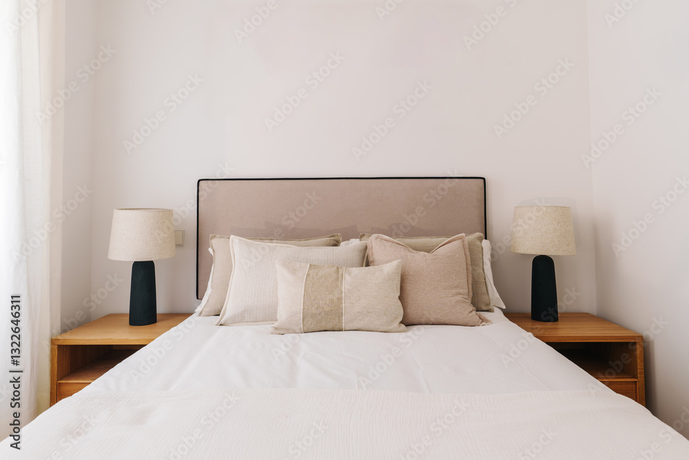 A neatly made double bed with beige and white pillows A neatly made double bed with beige and white pillows