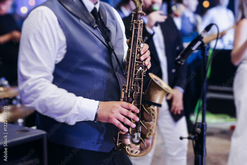 Fototapeta premium Concert view of saxophonist musician, saxophone sax player with vocalist and musical band during jazz orchestra show performing music on a stage in the scene lights, concert in a musical club hall