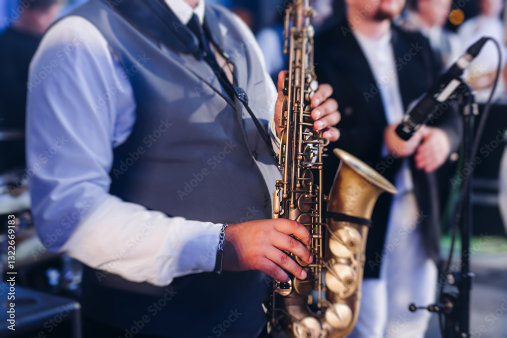 Fototapeta premium Concert view of saxophonist musician, saxophone sax player with vocalist and musical band during jazz orchestra show performing music on a stage in the scene lights, concert in a musical club hall