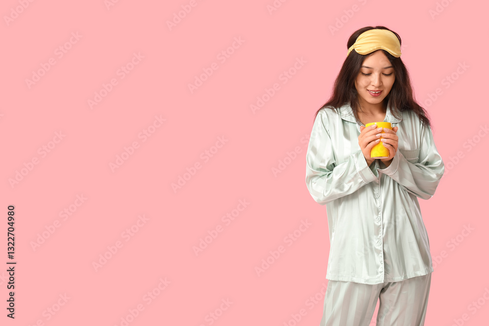 Beautiful young happy Asian woman in pajamas with sleeping mask and cup of coffee on pink background Beautiful young happy Asian woman in pajamas with sleeping mask and cup of coffee on pink background