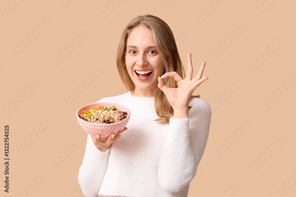 Young woman with bowl of healthy oatmeal showing OK on beige background