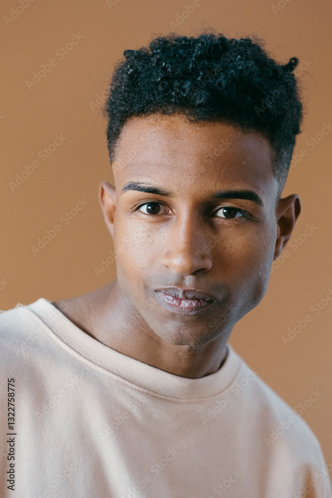© Jimena Roquero/Stocksy - Studio portrait of young man with curly hair looking at camera © Jimena Roquero/Stocksy - Studio portrait of young man with curly hair looking at camera