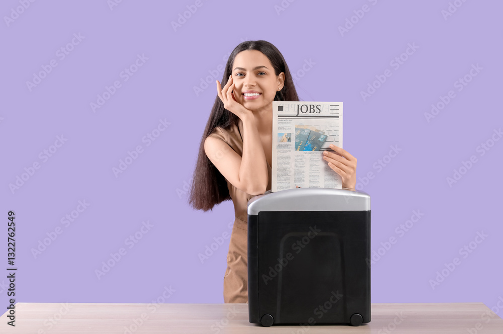 Happy young woman destroying newspaper using shredder on table against lilac background