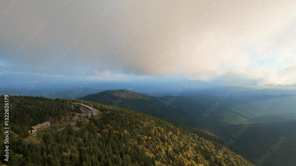 Aerial View of Mountain Landscape with Low-Hanging Clouds stunning aerial view of mountain range covered in dense forest, with misty clouds rolling over peaks under dramatic sky.