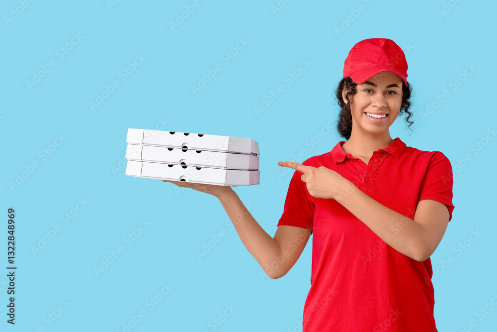 Female African-American courier pointing at cardboard boxes with tasty pizza on blue background Female African-American courier pointing at cardboard boxes with tasty pizza on blue background