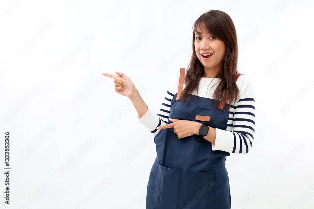 Asian waitress in blue apron pointing fingers sideways, showing advertisement and smiling excited, standing against white background.
