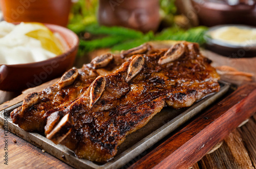 Short ribs, served on wood with blurred side dishes in the background. Assado de tira