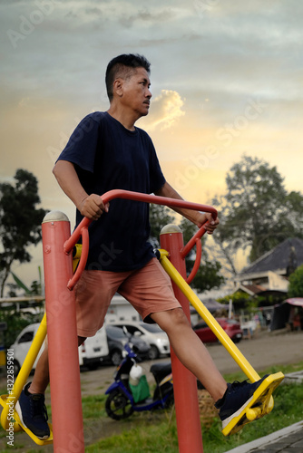 Side view of an Asian man using outdoors air walker exercise machine in public park