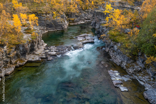 Golden autumn leaves near a blue river with a stone pathway in Norway