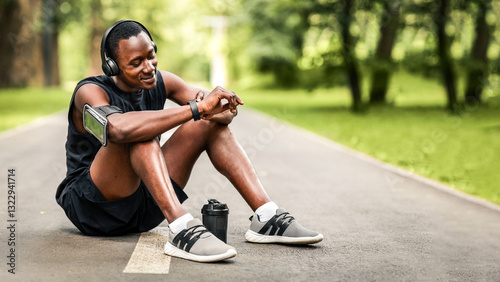 Athletic black man sitting on park way, checking on his smartwatch, measuring pulse, empty space
