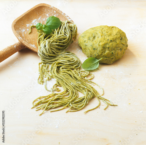 Homemade green spinach pasta is prepared on a wooden surface with fres