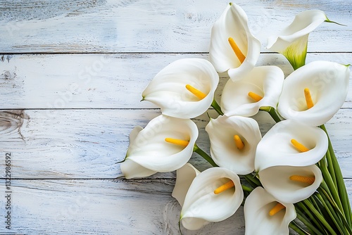White calla lilies arranged elegantly on a white wooden table, space for text