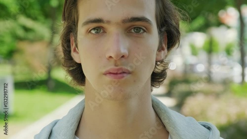 Unhappy alone young teenager, outdoors. Confident look. Young sad man looks on the camera.  Close up face of  handsome guy with sad eyes, in the nature.  Closeup  frustrated teenager face, outside.