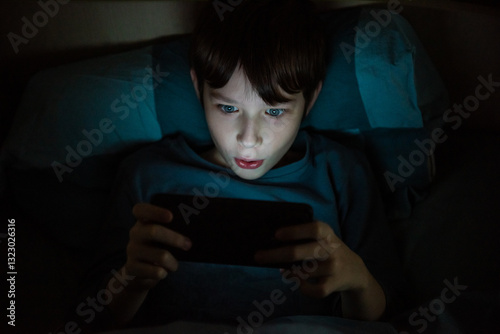 A teenage boy at night under a blanket with a phone. Children who are addicted to gadgets. Violation of mental health due to gadgets. Visual impairment.