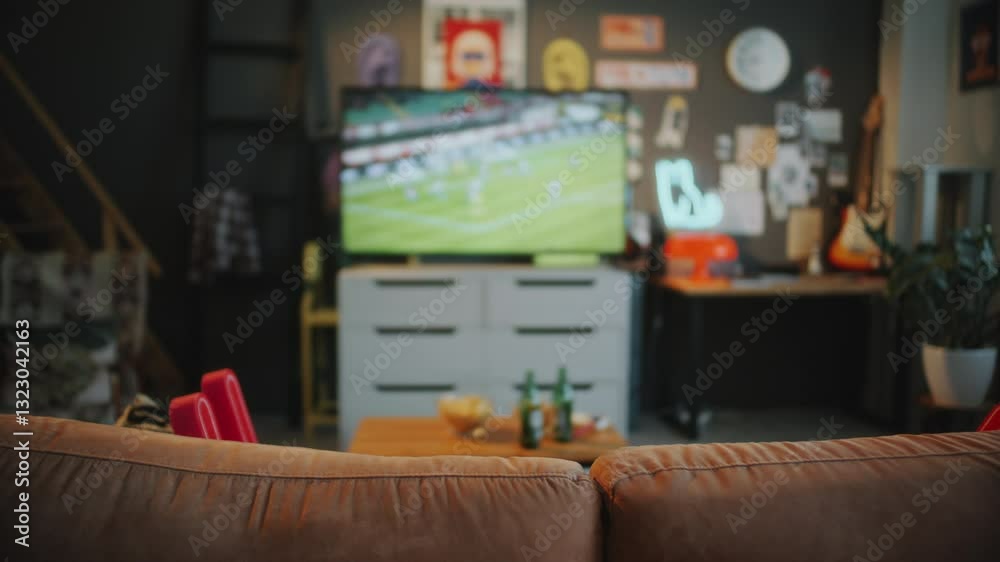 Empty living room with couch in foreground and TV displaying soccer match, coffee table with snacks and drinks in defocused background