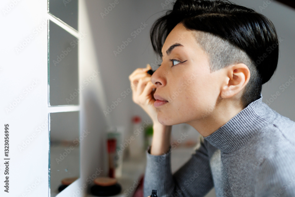 Woman in apartment bathroom applying eye liner in front of mirror Woman in apartment bathroom applying eye liner in front of mirror
