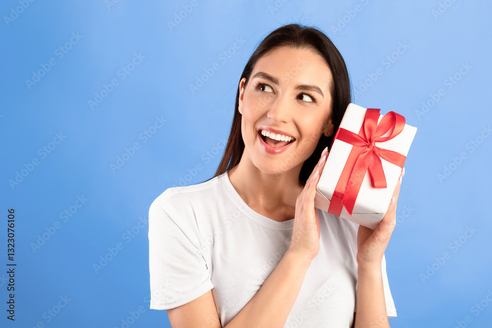 Guess What's Inside. Excited girl shaking present, listening what rattles in gift box, isolated over turquoise studio wall Guess What's Inside. Excited girl shaking present, listening what rattles in gift box, isolated over turquoise studio wall