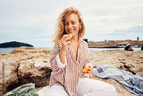 Happy woman eats an orange on the beach