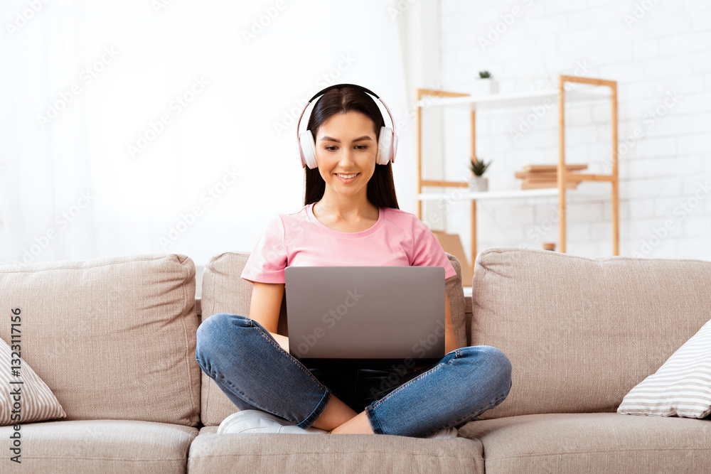 Home Office. Happy girl working on laptop sitting on the couch and listening to music in headphones, copyspace Home Office. Happy girl working on laptop sitting on the couch and listening to music in headphones, copyspace