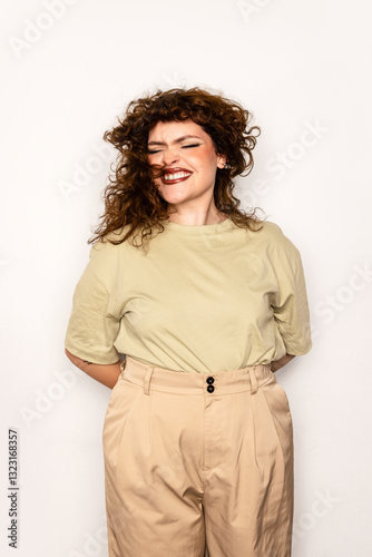 Joyful curvy woman with curly hair smiling in neutral outfit