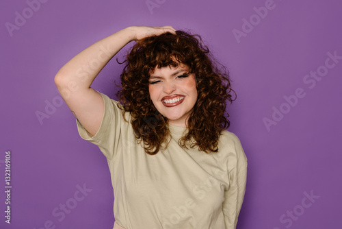 Joyful curvy woman with curly hair posing against purple background photo