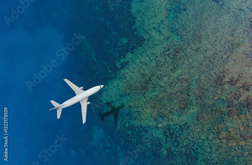 Airplane flying over clear blue ocean with reef visible below