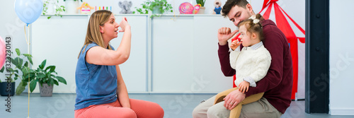 Foto Nonverbal child with Down syndrome learning baby sign language with the help of a speech therapist and her father