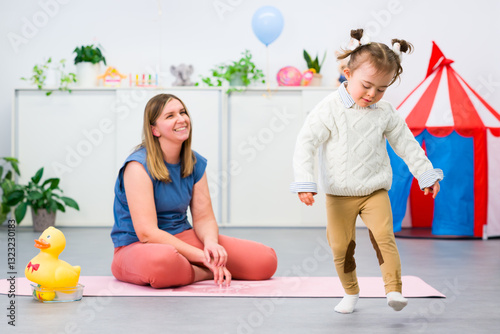 Toddler girl with Down syndrome in child occupational therapy session doing sensory playful exercises with her therapist. Child therapy, neurodiversity, learning difficulty, developmental disability.