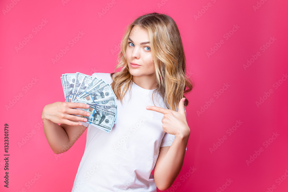 Financial Concepts. Winsome Caucasian Girl Posing WIth Bunch of American Currency Banknotes And Pointing With Finger Against Coral Background.
