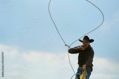 Cowboy skillfully swinging a lasso under a clear blue sky during a rodeo event. Brandenburg, Germany photo