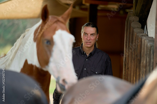 Man standing near horses in a stable, one prominently in the foreground. Brandenburg, Germany photo