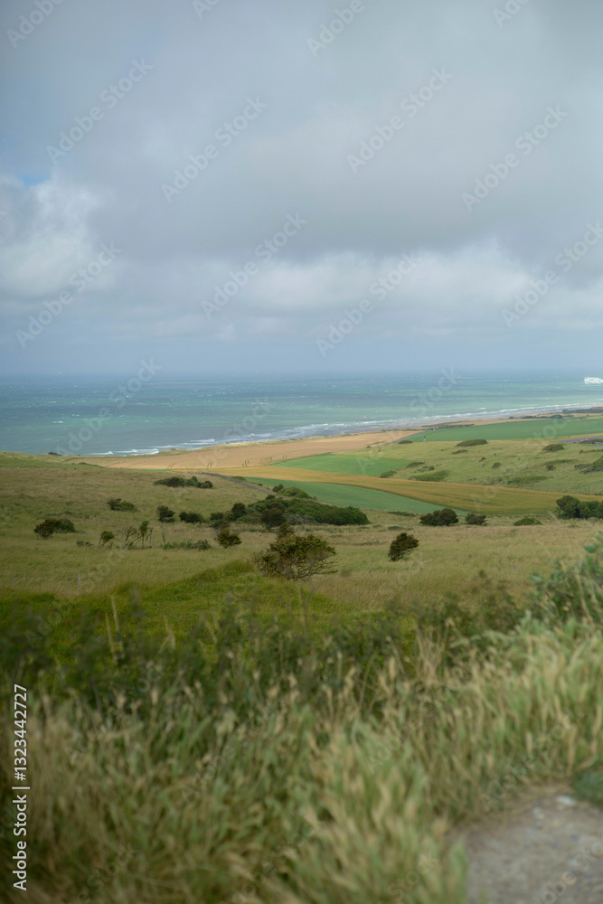 Rolling grassy hills leading to a sandy beach and distant ocean under a cloudy sky. Hauts-de-France, France Rolling grassy hills leading to a sandy beach and distant ocean under a cloudy sky. Hauts-de-France, France