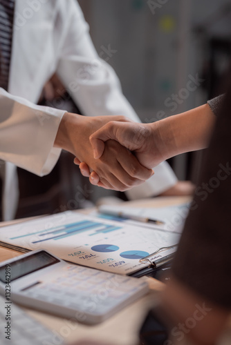 Doctors and managers shaking hands after a successful financial deal, with charts and calculator on the table, celebrating partnership and healthcare investment