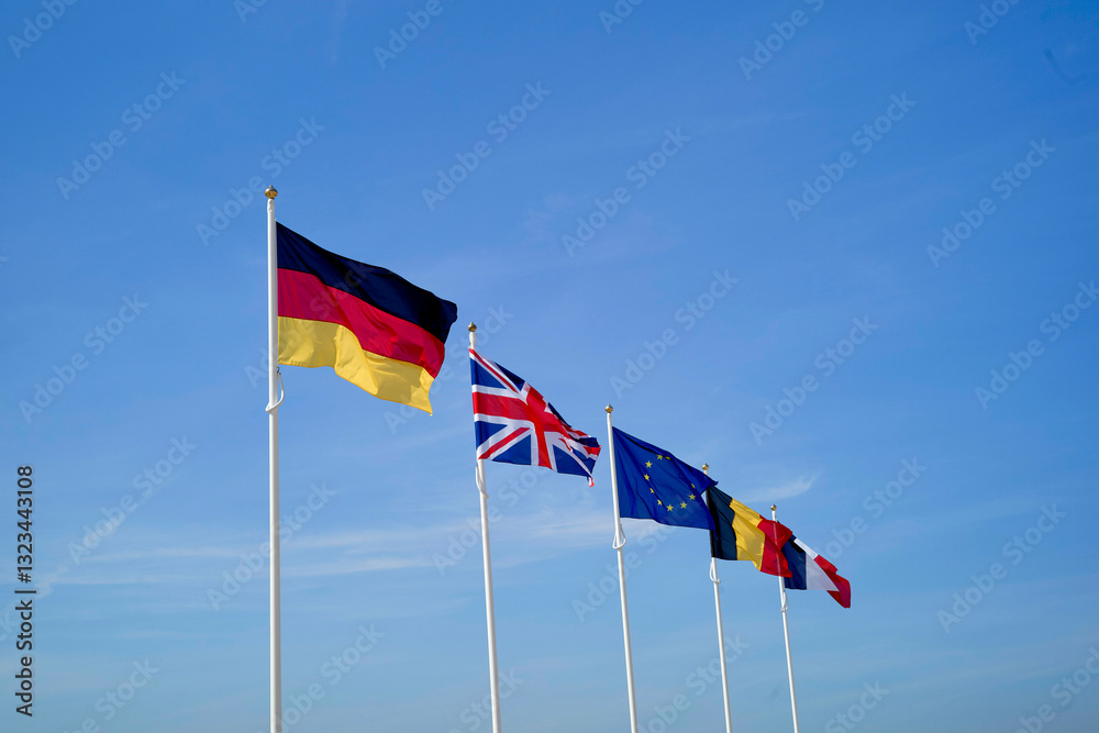 Five flags representing Germany, UK, EU, France, and Belgium waving against a clear blue sky. Hauts-de-France, France Five flags representing Germany, UK, EU, France, and Belgium waving against a clear blue sky. Hauts-de-France, France