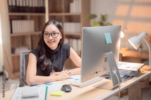 Wallpaper Mural Young Asian businesswoman smiling and working with desktop computer in office, she is analyzing financial chart and graph using computer at her desk in a modern office Torontodigital.ca