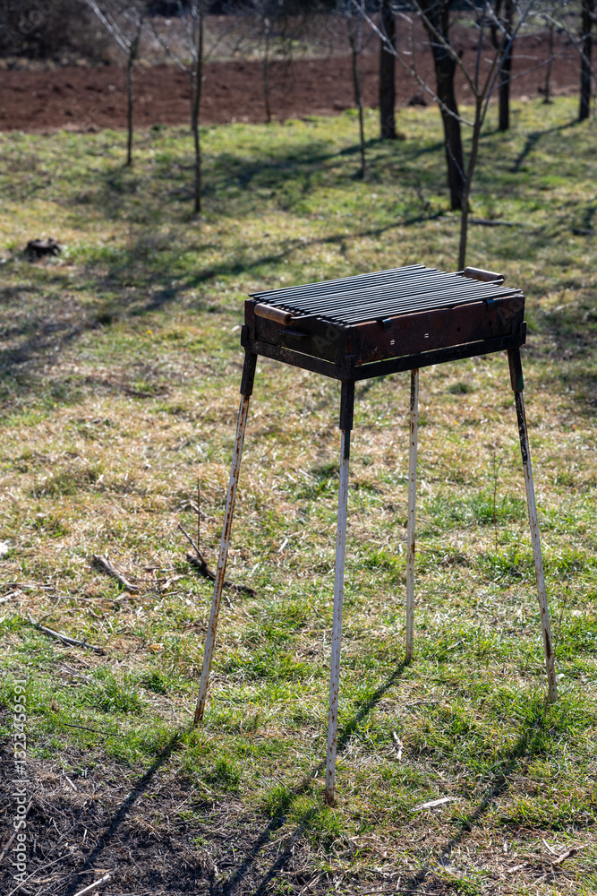 The old barbecue grill is set up in a country yard surrounded by plants and green grass. Metal grate for grilling.
The old barbecue grill is set up in a country yard surrounded by plants and green grass. Metal grate for grilling.