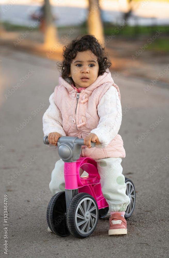 Portrait of cute toddler latin girl riding pink balance bike in park Portrait of cute toddler latin girl riding pink balance bike in park